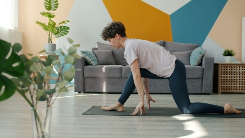 Person gör en stretchövning på yogamatta i ett ljust vardagsrum